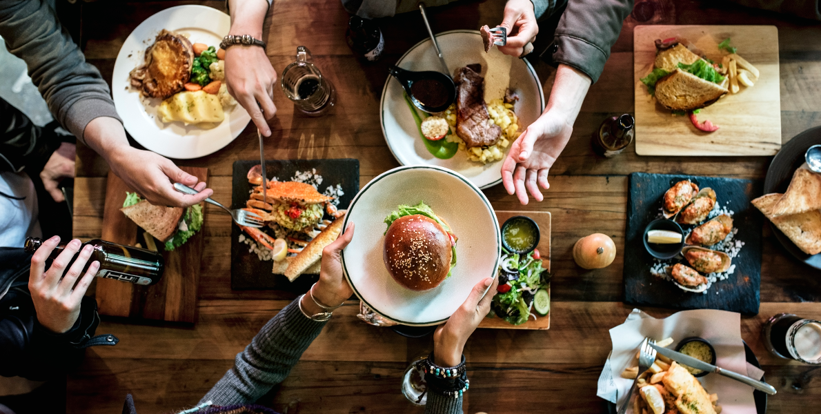 Fællesspisning af bord med lækker mad set fra fugleperspektiv. En person rækker en tallerken med mad til anden person