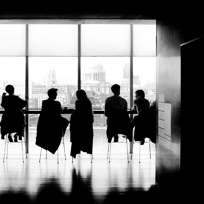 sort hvid billede af folk der sidder i et møde med ansigtet rettet mod væggen der er et gulv til loft vindue